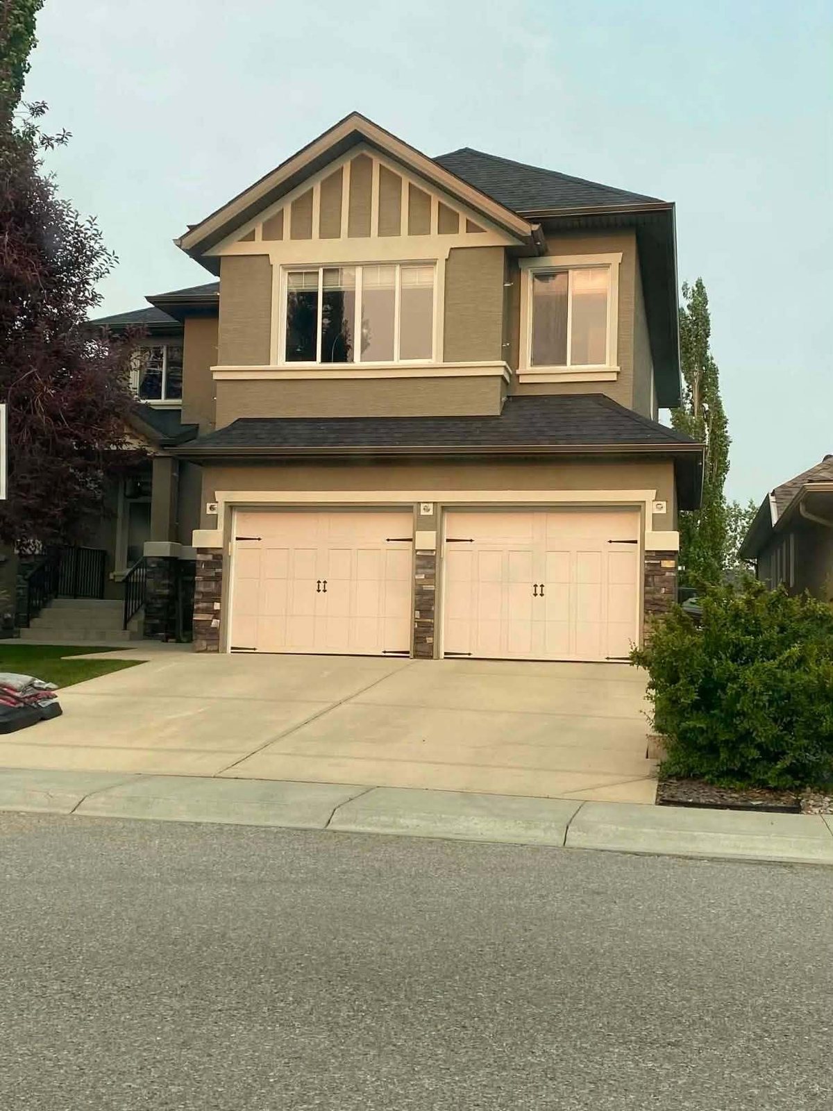 Two-storey home in olive and tan after a full exterior repaint, seen from the street