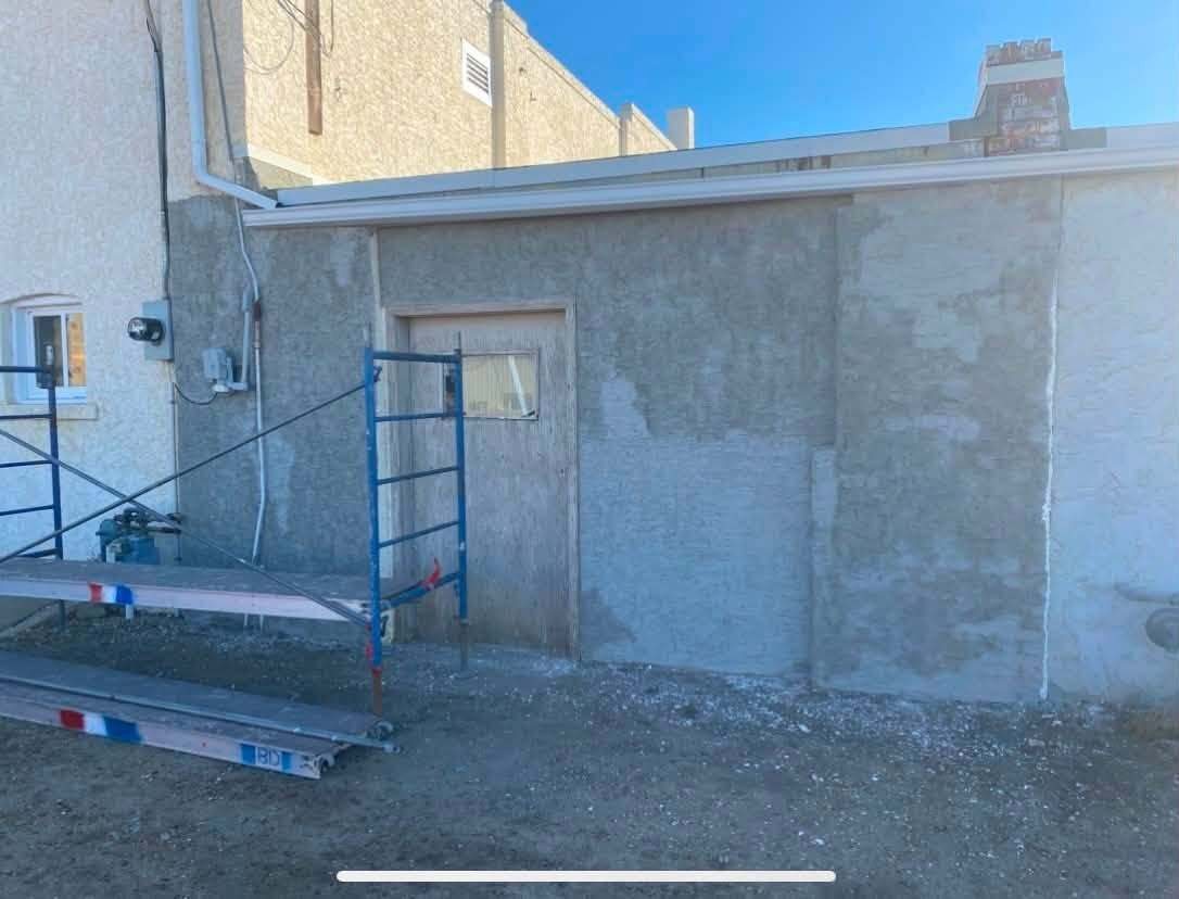 Before: commercial stucco exterior in patchy grey, with scaffolding up